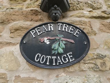A black oval sign with pears hanging from a branch and the text Pear Tree Cottage on a stone wall at Peartree Cottage in Stanford Bishop near Bromyard