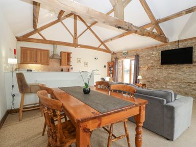 A living room and kitchen area with wooden dining table and chairs a gray sofa and exposed wooden ceiling beams at Peartree Cottage in Stanford Bishop near Bromyard