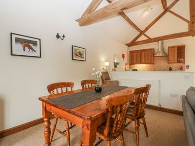 A dining area with a wooden table and chairs next to a kitchen with wooden cabinets at Peartree Cottage Stanford Bishop near Bromyard