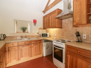 A kitchen with wooden cabinets a stove microwave knife set and a sink at Peartree Cottage Stanford Bishop near Bromyard