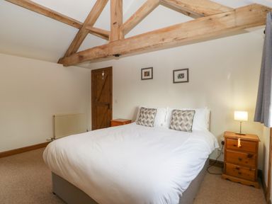 A bedroom with a double bed two wooden nightstands a lamp wooden door and exposed wooden ceiling beams at Peartree Cottage in Stanford Bishop near Bromyard