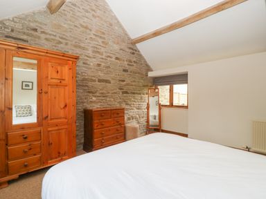 A bedroom with a wooden wardrobe a chest of drawers a standing mirror and a window at Peartree Cottage Stanford Bishop near Bromyard