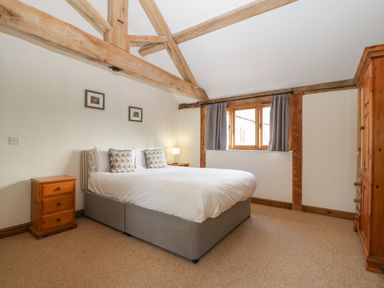 A bedroom with a double bed two wooden bedside tables a wooden wardrobe and exposed wooden beams at Peartree Cottage in Stanford Bishop near Bromyard