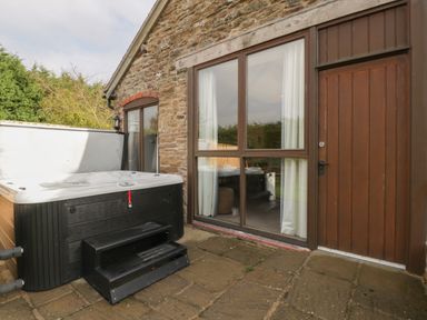 An outdoor patio with a hot tub beside a stone wall house with large window and wooden door at Peartree Cottage Stanford Bishop near Bromyard