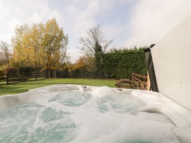 An outdoor hot tub with bubbling water in a grassy backyard with trees and a wooden fence at Peartree Cottage in Stanford Bishop near Bromyard