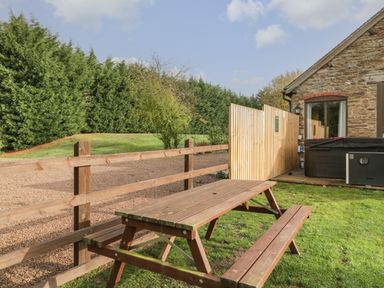 A wooden picnic table on grass near a stone building with a hot tub and wooden fence at Peartree Cottage Stanford Bishop near Bromyard