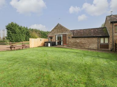 A stone house with a grassy yard and wooden picnic tables at Peartree Cottage in Stanford Bishop near Bromyard