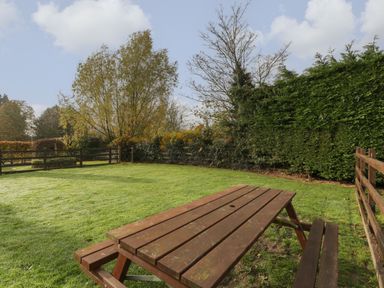 An outdoor green lawn with a wooden picnic table and fenced trees at Peartree Cottage Stanford Bishop near Bromyard
