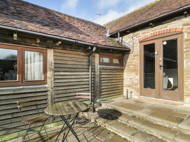 A small outdoor patio with wooden table and two chairs next to stone steps and a wooden and stone building at Peartree Cottage in Stanford Bishop near Bromyard