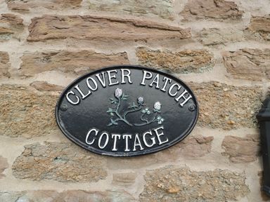 A stone wall with a black oval sign reading Clover Patch Cottage