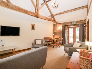 A living room with exposed wooden beams a dining table chairs two armchairs a sofa and a wall-mounted TV at Clover Patch Cottage Stanford Bishop near Bromyard
