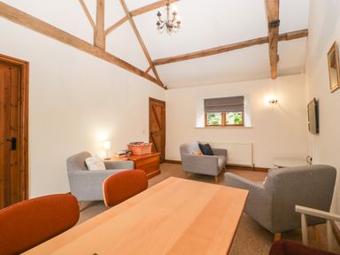A sitting room with wooden beams gray armchairs a wooden table and doors at Clover Patch Cottage Stanford Bishop near Bromyard