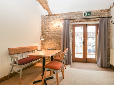 A dining area with a wooden table two chairs a bench and stone wall with a door and curtains at Clover Patch Cottage Stanford Bishop near Bromyard