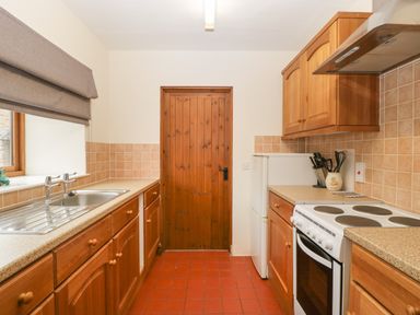 A kitchen with wooden cabinets a stove a sink and a wooden door at Clover Patch Cottage in Stanford Bishop near Bromyard