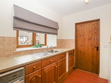 A kitchen with wooden cabinets a stainless steel sink a window with gray blinds and a wooden door at Clover Patch Cottage in Stanford Bishop near Bromyard