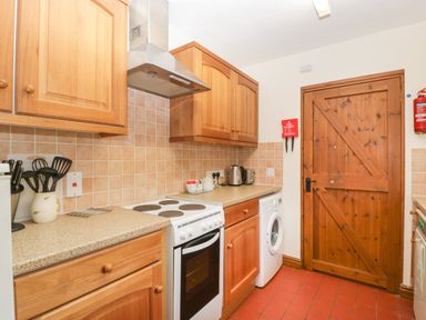 A kitchen with wooden cabinets stove washing machine and wooden door at Clover Patch Cottage Stanford Bishop near Bromyard
