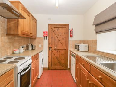 A kitchen with wooden cabinets a white stove washing machine microwave and a wooden door at Clover Patch Cottage Stanford Bishop near Bromyard