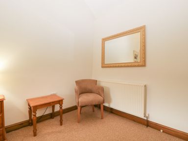 A small room with a brown upholstered chair wooden tables and a wall mirror at Clover Patch Cottage in Stanford Bishop near Bromyard