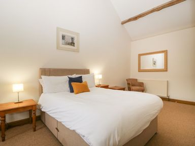 A bedroom with a double bed pillows side tables lamps a chair and a mirror on the wall at Clover Patch Cottage in Stanford Bishop near Bromyard