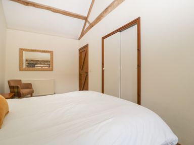 A bedroom with a white bed a brown chair a wooden door and a large mirror at Clover Patch Cottage Stanford Bishop near Bromyard