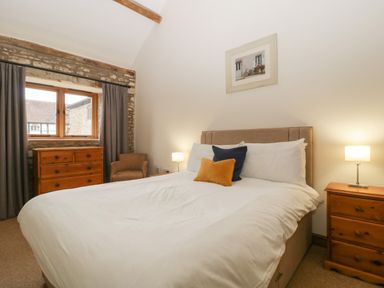 A bedroom with a bed with pillows bedside tables with lamps a chest of drawers an armchair and a window at Clover Patch Cottage in Stanford Bishop near Bromyard