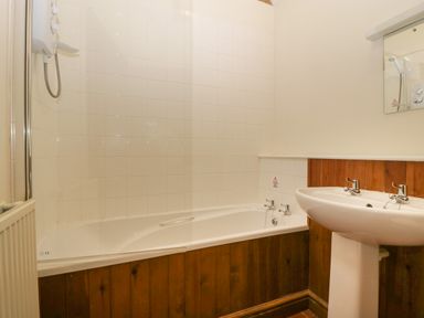 A bathroom with a bathtub and shower next to a pedestal sink with taps at Clover Patch Cottage Stanford Bishop near Bromyard