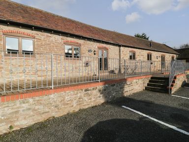Exterior view of a stone building with a tiled roof and metal railing along a raised wooden deck at Clover Patch Cottage in Stanford Bishop near Bromyard