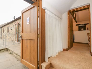 A hallway with an open wooden door leading outside to a stone patio and a stone building at Honeysuckle Cottage in Stanford Bishop near Bromyard