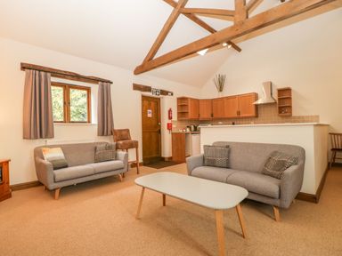A living room area with two gray sofas and a coffee table in front of a kitchen with wooden cabinets and exposed wooden ceiling beams at Honeysuckle Cottage Stanford Bishop near Bromyard