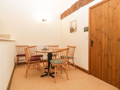 A dining area with a round table and six wooden chairs near a wooden door at Honeysuckle Cottage Stanford Bishop near Bromyard
