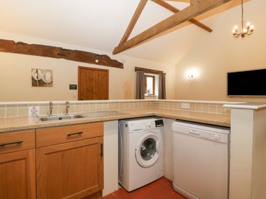 A kitchen area with wooden cabinets a washing machine dishwasher sink and exposed wooden beams at Honeysuckle Cottage in Stanford Bishop near Bromyard