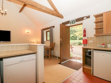 A kitchen area with a dishwasher fridge open door showing an outdoor area and a chair near a window at Honeysuckle Cottage Stanford Bishop near Bromyard