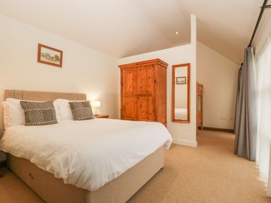 A bedroom with a double bed two pillows a wooden wardrobe a mirror and bunk beds at Honeysuckle Cottage in Stanford Bishop near Bromyard