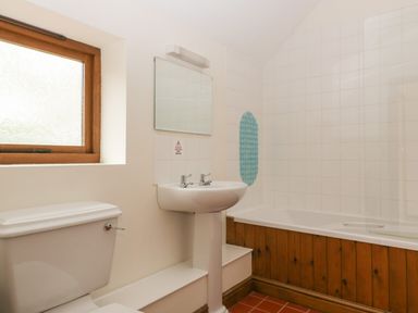 A bathroom with a toilet sink and bathtub with wooden paneling and a frosted window at Honeysuckle Cottage Stanford Bishop near Bromyard