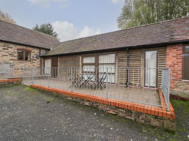 A tiled patio with metal railing and outdoor furniture in front of a single story building with wooden and brick walls at Honeysuckle Cottage Stanford Bishop near Bromyard