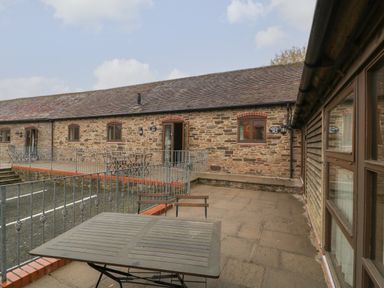 An outdoor patio area with tables and chairs in front of a stone building at Honeysuckle Cottage Stanford Bishop near Bromyard