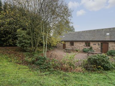 A stone building with wooden doors and windows surrounded by grass trees and picnic benches at Honeysuckle Cottage Stanford Bishop near Bromyard