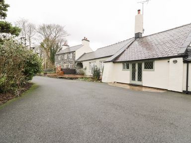 Exterior view of a stone and white painted house with slate roof and driveway at Lakeside Cottage in Llanrug