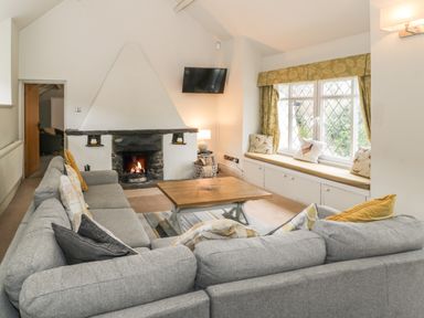 A living room with a grey sofa around a wooden coffee table a fireplace a wall-mounted TV and window seating at Lakeside Cottage in Llanrug