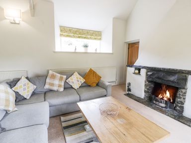 A living room with a grey sofa cushions wooden coffee table and a fireplace at Lakeside Cottage in Llanrug