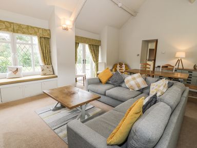 A living room with gray sofas a wooden coffee table and a dining table with chairs at Lakeside Cottage in Llanrug