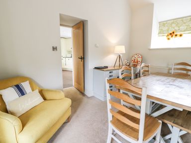 A dining room with wooden table and chairs a yellow sofa and a lamp on a side cabinet at Lakeside Cottage in Llanrug