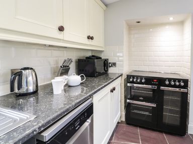 A kitchen with a black stove oven microwave kettle tea set and knives at Lakeside Cottage in Llanrug