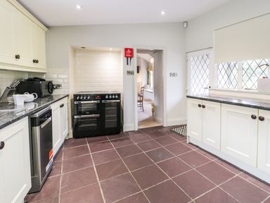A kitchen with cream cabinets black countertops a black stove and a window with a roller blind at Lakeside Cottage in Llanrug