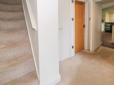 A hallway with carpeted stairs a wooden door and a view into a kitchen at Lakeside Cottage in Llanrug