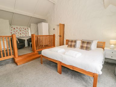 A bedroom with a wooden bed with pillows and towels a white wardrobe two armchairs and a small table at Lakeside Cottage in Llanrug