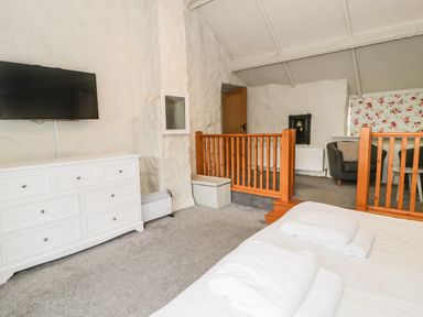 A bedroom with a white dresser and a wall-mounted TV with a wooden railing separating a seating area at Lakeside Cottage in Llanrug