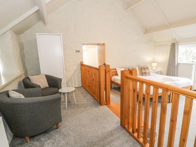 A bedroom with a double bed a small sitting area with two armchairs a white wardrobe and a wooden railing at Lakeside Cottage in Llanrug