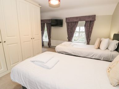 A bedroom with two single beds white wardrobes and windows with curtains at Lakeside Cottage in Llanrug