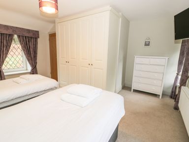 A bedroom with two beds white wardrobes a white chest of drawers and purple curtains at Lakeside Cottage in Llanrug